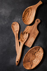 Olive wood kitchen utensils with chopping board and bowl on stone table background. Top view. Space for text