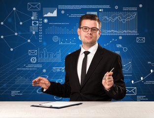 Young handsome businessman sitting at a desk with blue charts and data behind him