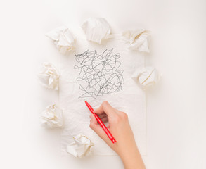 Female hand next to a few crumpled paper balls drawing random scribbles 