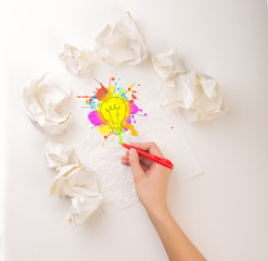 Female hand next to a few crumpled paper balls drawing a colorful lightbulb