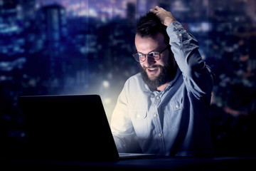 Young handsome businessman working late at night in the office with blue lights in the background