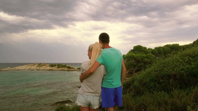 Young couple - man and girl, embracing, looking at the stormy sea, Greece