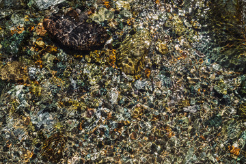 Varicolored detailed texture of stony bottom of transparent brook close up. Clean water in mountain creek. Colorful background of smooth stones in river stream with copy space.
