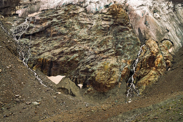 Detailed natural texture of giant rock of fantastic shape covered with snow and ice in highlands. Small waterfalls and brooks flow down mountainside. Fantasy mountain landscape of majestic nature.