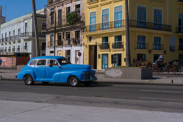 Fototapeta na wymiar Un carro muy viejo de color azul realiza trabajo de taxi por el casco histórico de la Habana.