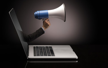 Hand with loudspeaker coming out of a laptop with sparkling effects
