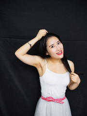 Portrait of good looking sexy Chinese woman with long black hair and white halter against black...