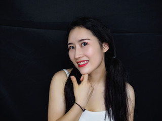 Portrait of good looking sexy Chinese woman with long black hair and white halter against black...