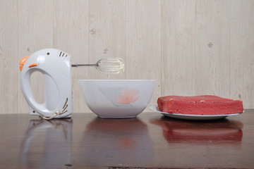Whipped cream in glass bowl and mixer on wooden table for making  a red velvet cake.