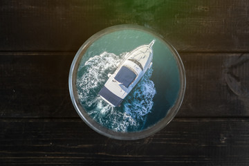 hand holding a cup on wooden table with boat in the sea inside a creative concept idea