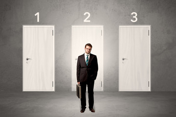 Businessman in grey room with three numbered white  door behind his back
