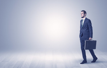 Successful businessman walking in front of an empty wall with briefcase on his hand
