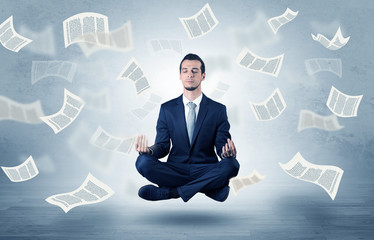 Young businessman meditating with documents and papers flying around him
