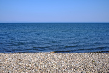 Fototapeta na wymiar Beach with stones on sand on background of blue sky.