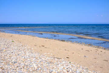 Fototapeta na wymiar Beach with stones on golden sand on background of blue sky.