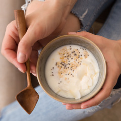 Top view on young woman's hands holding bowl with homemade organic vanilla yogurt with chia seeds. Girl eating smoothie bowl.