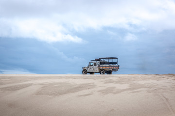 A old truck driving through the unique white sand dunes in a cloud day in the Lencois Maranhenses in north Brazil