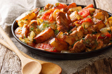 Home-style food: fried meat with potatoes, tomatoes, onions, herbs and spices close-up on a frying pan on a table. horizontal