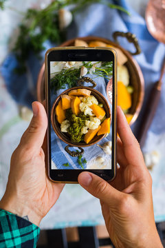 Woman hands takes photography of food on table with phone. Dinner, lunch. Cooked steam vegetables. Smartphone photo for social networks or blogging post. Vegetarian, healthy, organic