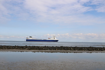 Fototapeta na wymiar Steinwall trennt Wattenmeer von der offenen Nordsee mit Fahrrinne für Schifffahrt vor Cuxhaven