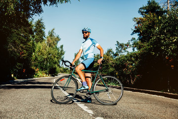 Fototapeta premium A man with a bicycle in the mountains. Road in the mountains covered with forest.