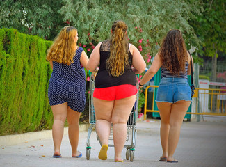 three fat girls are taking food in a basket from a supermarket down the street. view from the back