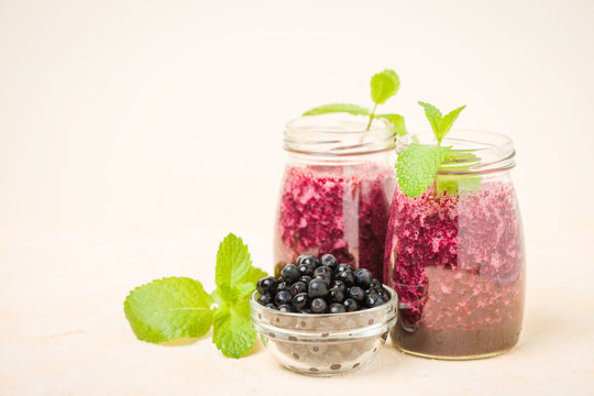 Blueberry smoothie decorated with fresh green mint leaves and raw ripe berries on yellow pastel background.