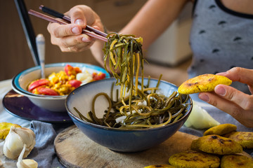 Woman hand takes and twirls with chopsticks a chuka laminaria seaweed salad with lime, lemon juice, garlic, onion on plate. Traditional Japanese, Chinese, Korean asian seafood. Healthy vegan lunch