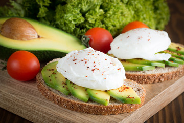 Avocado toast, cherry tomato and poached eggs on wooden background. Breakfast with vegetarian food, healthy diet concept.