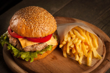 Home made hamburger with beef, onion, tomato, lettuce and cheese. Fresh burger close up on wooden rustic table with potato fries, beer and chips. Cheeseburger.