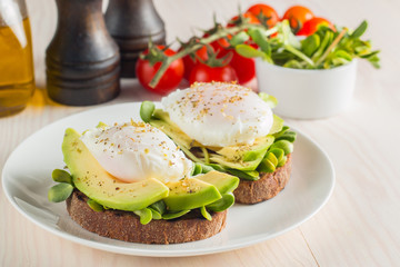 Avocado toast, cherry tomato and poached eggs on wooden background. Breakfast with vegetarian food, healthy diet concept.