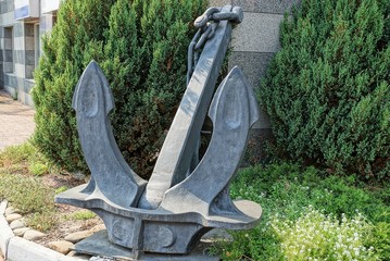 large black iron sea anchor in green grass and vegetation near the wall