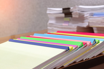 Close up pile of unfinished homework assignment on teacher's desk waiting to be inspected. Stack of paperwork separated by black paper clip and plastic binding bars. Education and business concept.