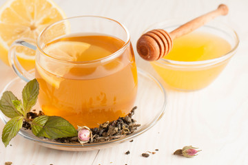 Closeup of cup of tea with tea leaves, mint on vintage wooden background. Black herbal tea with lemon, ginger and honey. hot winter drink