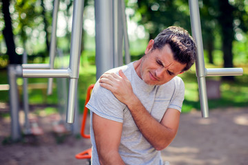 Obraz premium A man feeling pain in his shoulder during sport and workout in the park. Sport, medicine and people concept