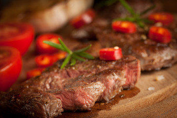 grilled fillet steak with tomatoes and roast vegetables on an old wooden board, background.