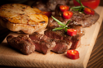 grilled fillet steak with tomatoes and roast vegetables on an old wooden board, background.