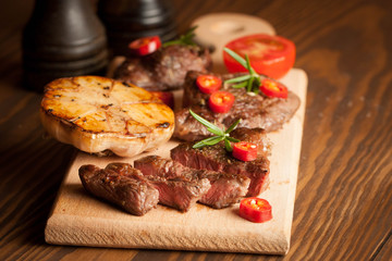 grilled fillet steak with tomatoes and roast vegetables on an old wooden board, background.