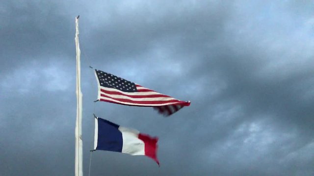American and French flags blowing in the wind under dark storm clouds