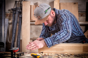 experienced carpenter in work clothes and small buiness owner measures a wooden board with a ruler and marks with pencil the necessary points for slices