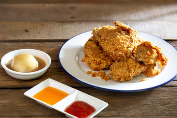 Fried chicken in white dish with souce and mash potato on wooden table.