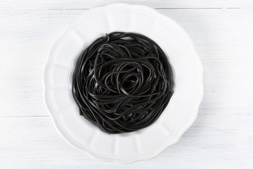 Pasta with wheat germ and black squid ink. Black pasta and parsley on a white plate. The background is white. Macro. Top view. Horizontal shot. Copy space.