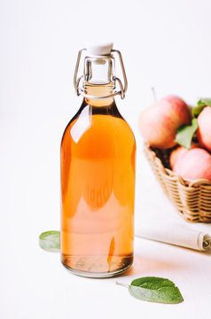 Apple vinegar in a bottle on white wooden table with apples in a basket.