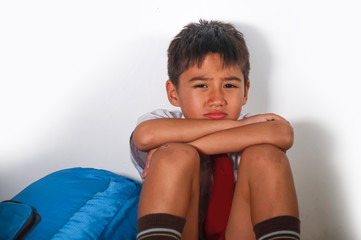 young sad scared latin kid 8 years old in school uniform and backpack sitting alone crying...