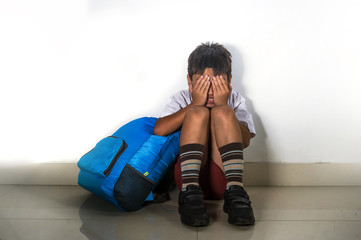  young sad and scared hispanic kid 8 years old in school uniform sitting alone crying depressed and...