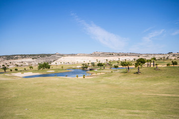 View of golf course with lake, sandpits and palm trees on a clear summer day in Spain