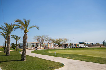 Fototapeta na wymiar Golf clubhouse with palm trees, buggies and putting green at golf course in Spain on a summer day with clear blue sky