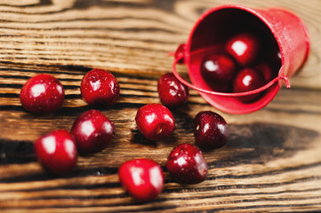 Fresh red cherries poured out of metal bucket on old brown wooden table. Agriculture concept