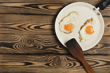 Two fried eggs in metal beige pan near dirty spatula on old wooden brown table. Top view with copy space