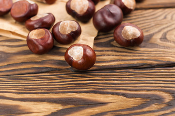Scattered smooth brown chestnuts and crumpled paper on old wooden rustic brown table with copy space for your text